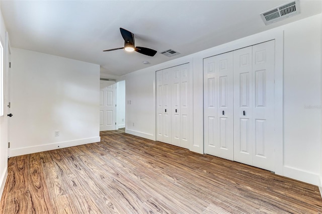 unfurnished bedroom with multiple closets, wood-type flooring, and ceiling fan