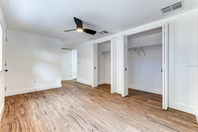 unfurnished bedroom with hardwood / wood-style flooring, ceiling fan, and multiple closets