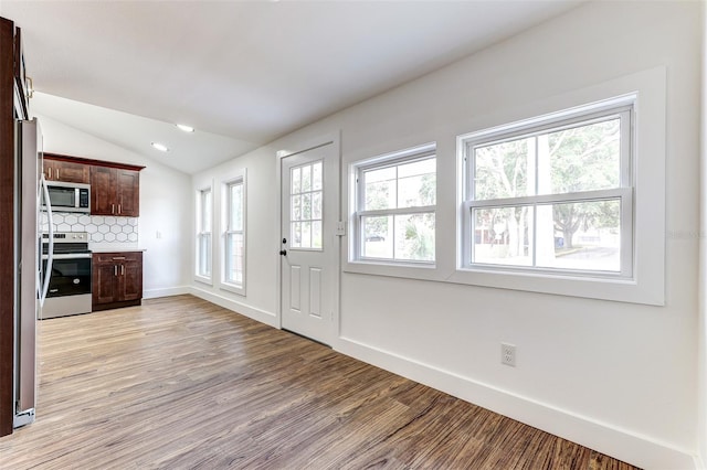 kitchen with light hardwood / wood-style floors, vaulted ceiling, dark brown cabinetry, backsplash, and appliances with stainless steel finishes