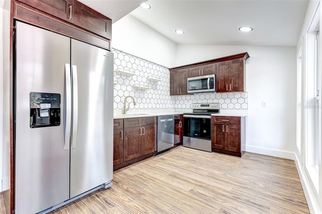 kitchen with stainless steel appliances, vaulted ceiling, light wood-type flooring, and backsplash