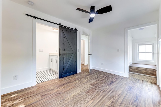 unfurnished bedroom with hardwood / wood-style floors, ensuite bathroom, a barn door, and ceiling fan