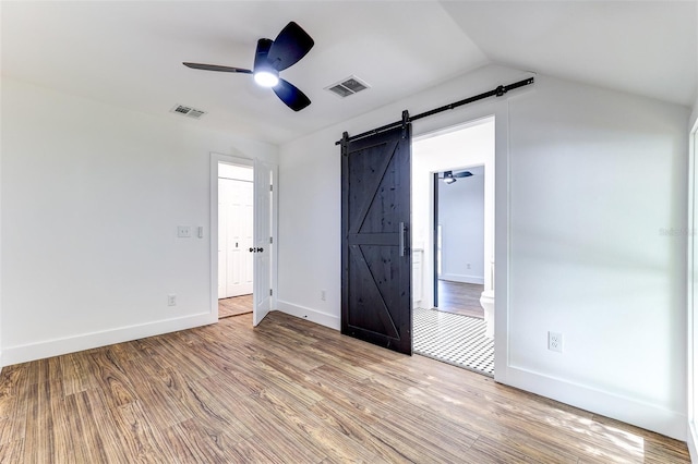 unfurnished bedroom featuring ceiling fan, a barn door, light hardwood / wood-style floors, and lofted ceiling