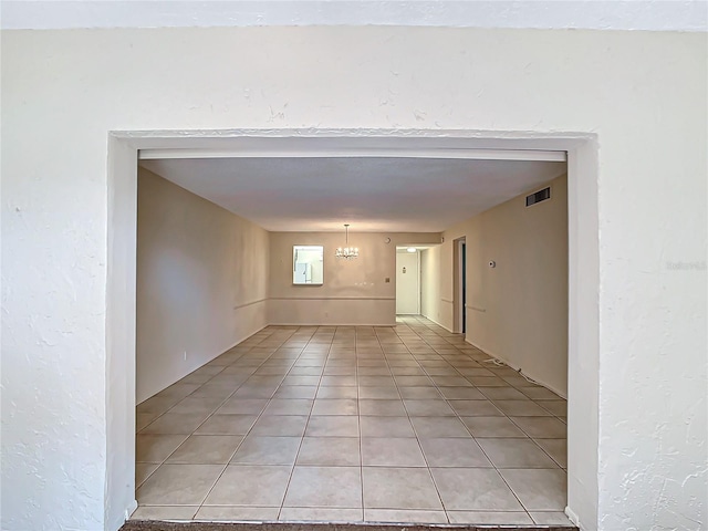 tiled empty room featuring an inviting chandelier