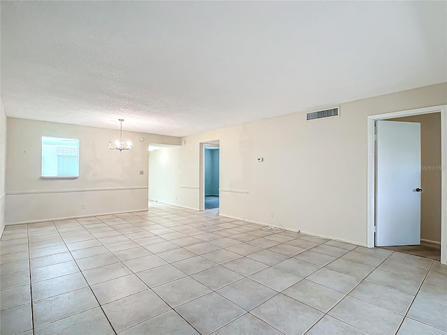 spare room featuring a chandelier, light tile patterned floors, and a textured ceiling