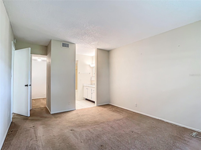 unfurnished bedroom featuring light colored carpet, a textured ceiling, and ensuite bathroom