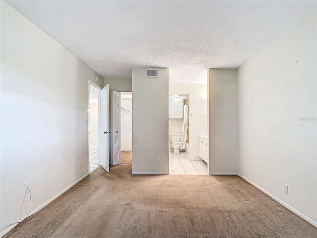 unfurnished bedroom with light colored carpet, connected bathroom, a closet, and a textured ceiling