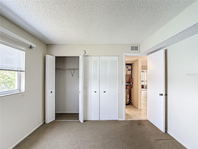 unfurnished bedroom featuring light colored carpet, a textured ceiling, and two closets