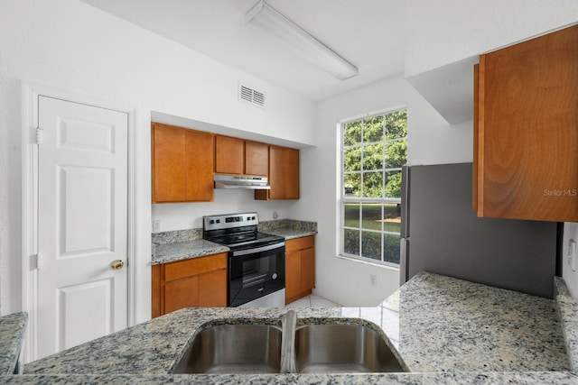 kitchen featuring light stone counters, sink, stainless steel fridge, and range with electric stovetop