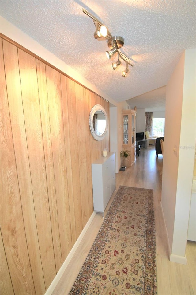 hallway with a textured ceiling, wood walls, and light wood-type flooring