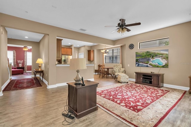 living room with ceiling fan with notable chandelier and light wood-type flooring