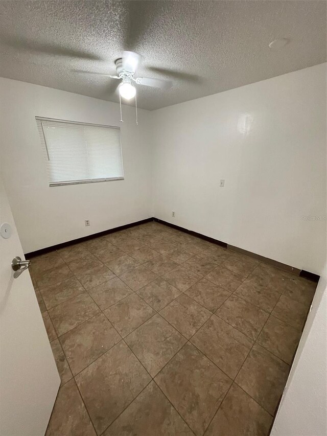 tiled empty room with ceiling fan and a textured ceiling