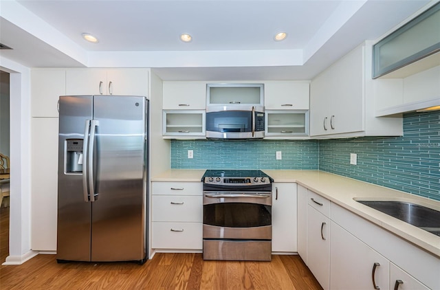 kitchen with backsplash, appliances with stainless steel finishes, light wood-type flooring, and white cabinets