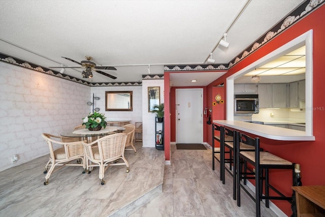 tiled dining room featuring track lighting, ceiling fan, and a textured ceiling