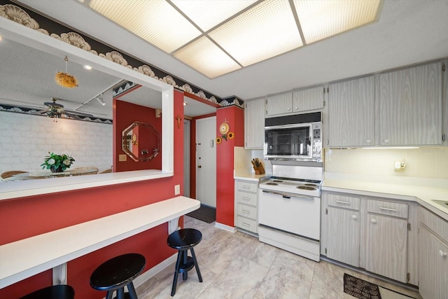 kitchen with white range with electric stovetop, light tile flooring, backsplash, ceiling fan, and stainless steel microwave