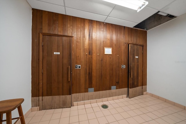 interior space featuring tile flooring, wood walls, and a drop ceiling