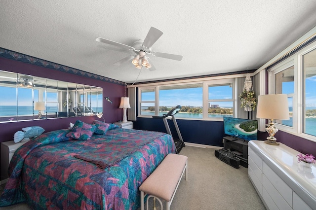 carpeted bedroom featuring a water view, ceiling fan, and a textured ceiling