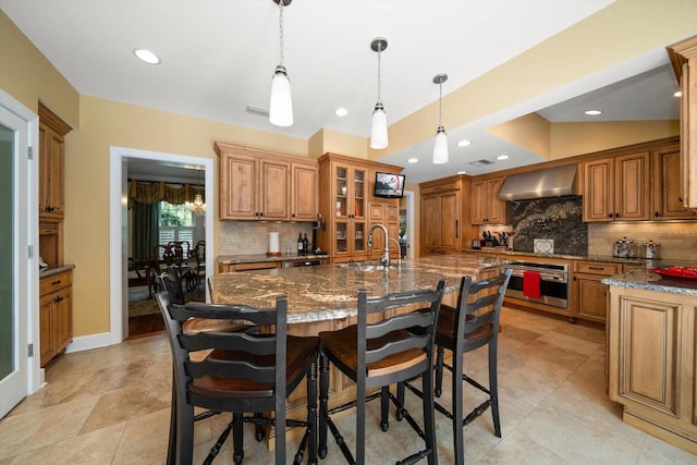 kitchen with hanging light fixtures, oven, wall chimney range hood, and tasteful backsplash