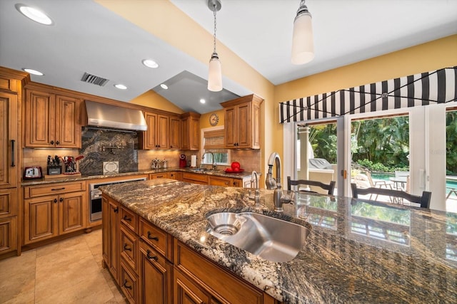 kitchen featuring wall chimney range hood, hanging light fixtures, tasteful backsplash, sink, and light tile floors