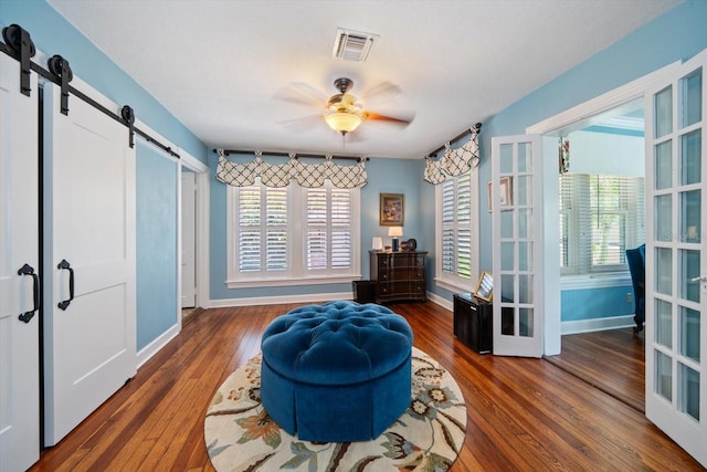 sitting room with a barn door, ceiling fan, french doors, and hardwood / wood-style flooring