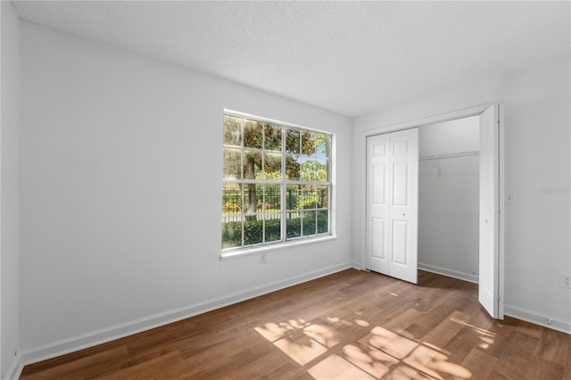 unfurnished bedroom with a textured ceiling, dark hardwood / wood-style floors, and a closet