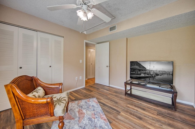 living area with hardwood / wood-style floors, ceiling fan, and a textured ceiling