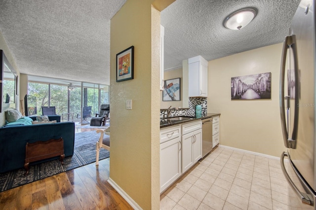 kitchen featuring a textured ceiling, appliances with stainless steel finishes, white cabinets, expansive windows, and sink