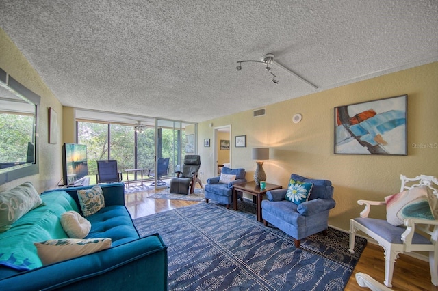 living room featuring a textured ceiling, wood-type flooring, and a wall of windows