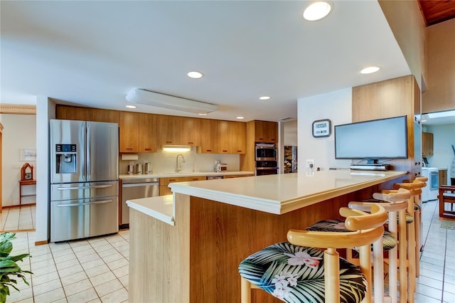 kitchen with sink, stainless steel appliances, backsplash, a breakfast bar, and light tile patterned floors