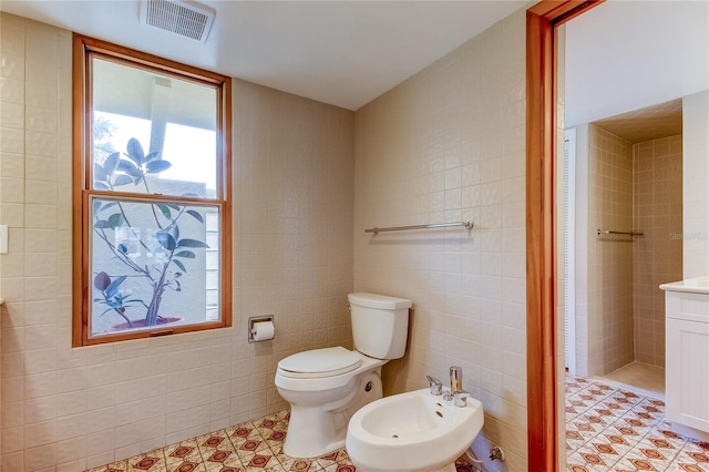 bathroom with vanity, a bidet, tile walls, tile patterned flooring, and toilet