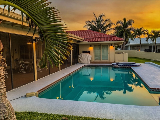 pool at dusk featuring area for grilling and an in ground hot tub