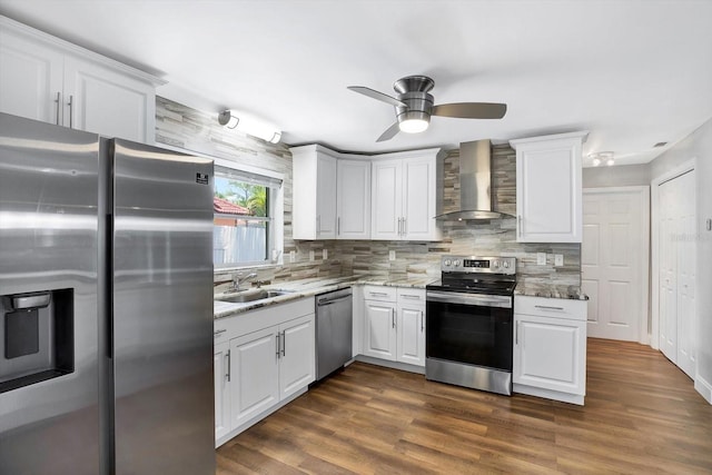 kitchen featuring stainless steel appliances, light stone counters, wall chimney exhaust hood, white cabinets, and sink