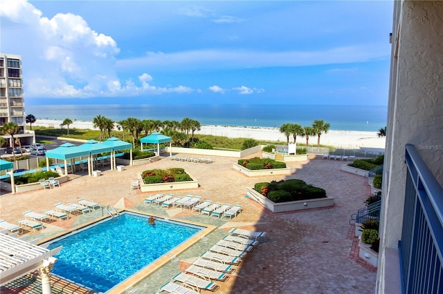 view of swimming pool featuring a patio area, a water view, and a beach view