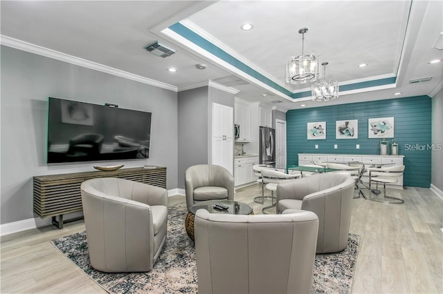 living room featuring a chandelier, a tray ceiling, ornamental molding, and light hardwood / wood-style floors