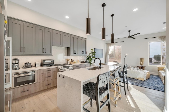 kitchen with gray cabinetry, sink, stainless steel appliances, hanging light fixtures, and a breakfast bar