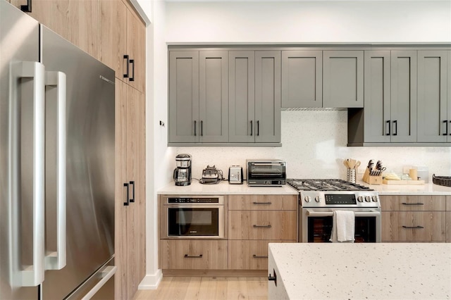 kitchen featuring light stone countertops, appliances with stainless steel finishes, decorative backsplash, light hardwood / wood-style flooring, and gray cabinets