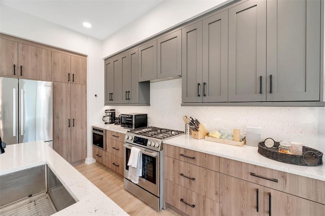 kitchen featuring light stone countertops, decorative backsplash, stainless steel appliances, sink, and light hardwood / wood-style floors