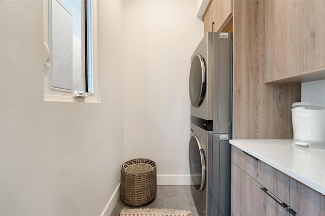 clothes washing area with cabinets, light tile patterned floors, and stacked washer and dryer