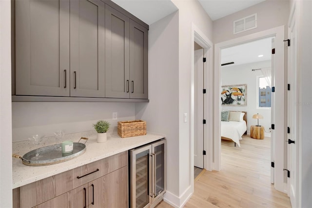 bar with light wood-type flooring, light stone countertops, and beverage cooler