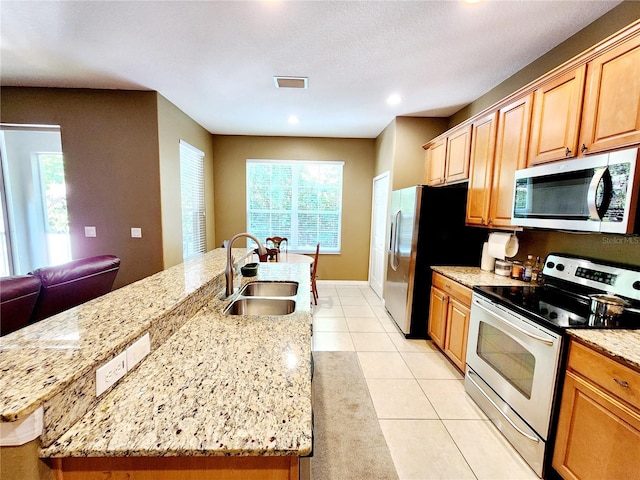 kitchen featuring sink, light tile patterned floors, appliances with stainless steel finishes, light stone counters, and an island with sink