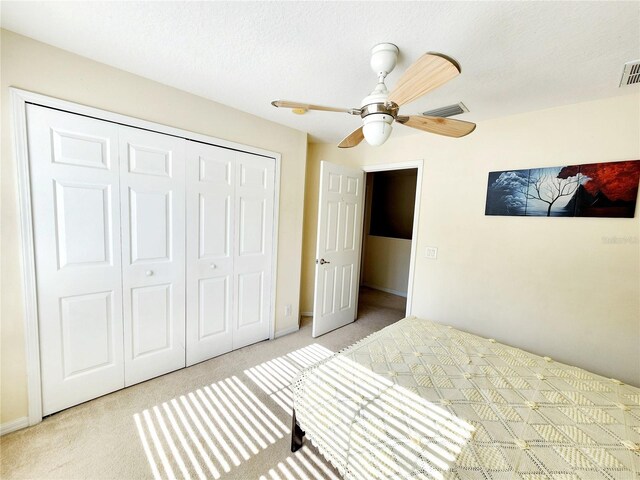 bedroom featuring light colored carpet, a textured ceiling, ceiling fan, and a closet