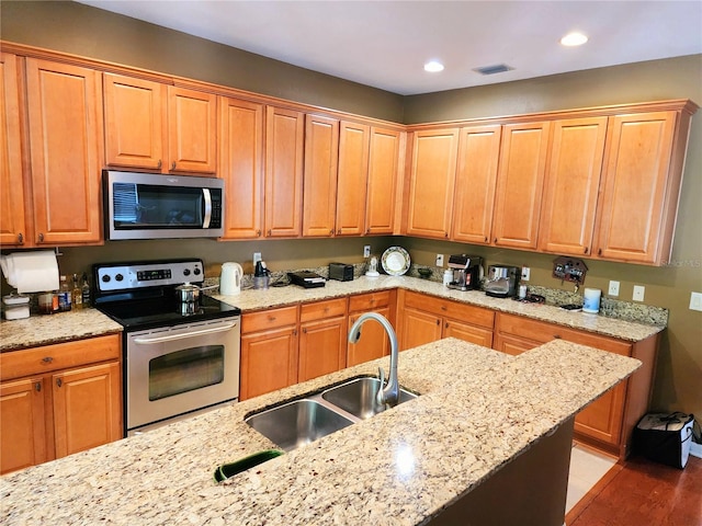 kitchen with appliances with stainless steel finishes, light wood-type flooring, light stone counters, and sink