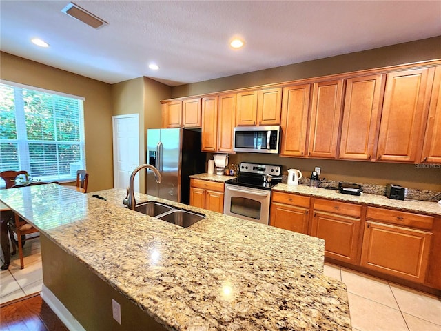 kitchen featuring light stone countertops, appliances with stainless steel finishes, sink, light tile patterned floors, and an island with sink