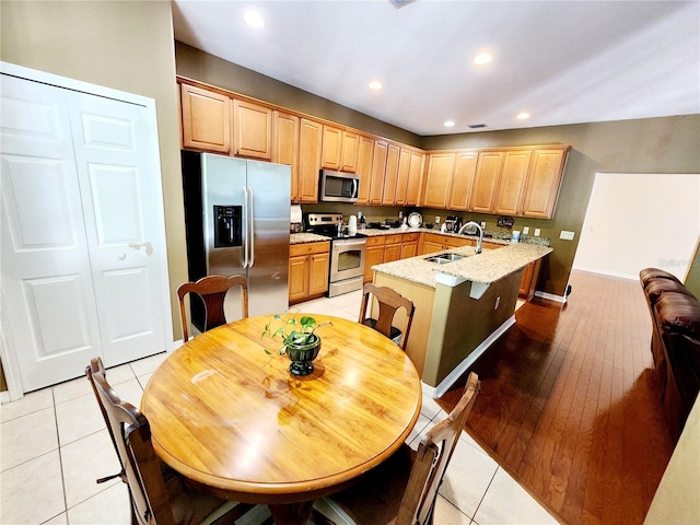 kitchen with light stone counters, stainless steel appliances, sink, light tile patterned floors, and a center island with sink