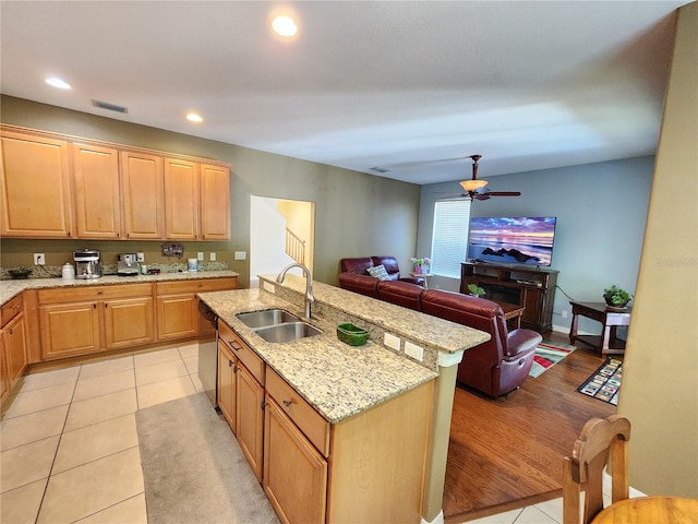 kitchen with light stone countertops, dishwasher, sink, an island with sink, and light wood-type flooring