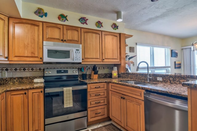 kitchen featuring appliances with stainless steel finishes, a textured ceiling, sink, light tile patterned floors, and dark stone countertops