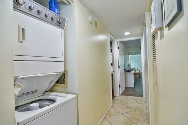 clothes washing area featuring light tile patterned floors and stacked washing maching and dryer