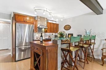 kitchen with light hardwood / wood-style flooring, stainless steel fridge, track lighting, a center island, and wall chimney exhaust hood