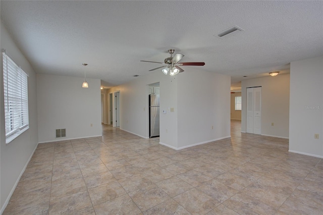 tiled empty room with ceiling fan and a textured ceiling