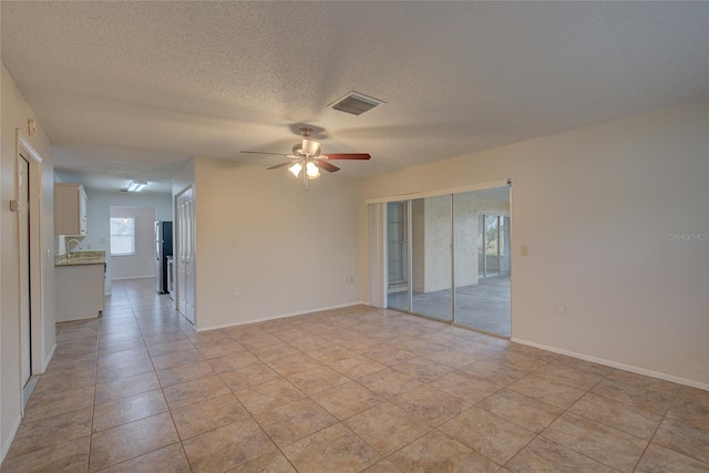 tiled empty room featuring a textured ceiling and ceiling fan