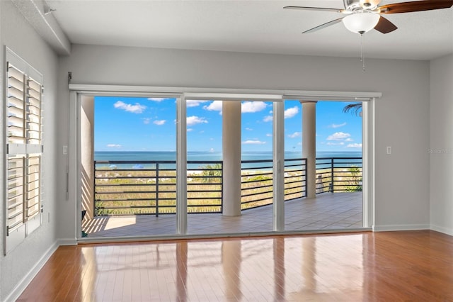 spare room featuring a healthy amount of sunlight, wood-type flooring, ceiling fan, and a water view